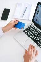 A person looking at their credit card while using their laptop