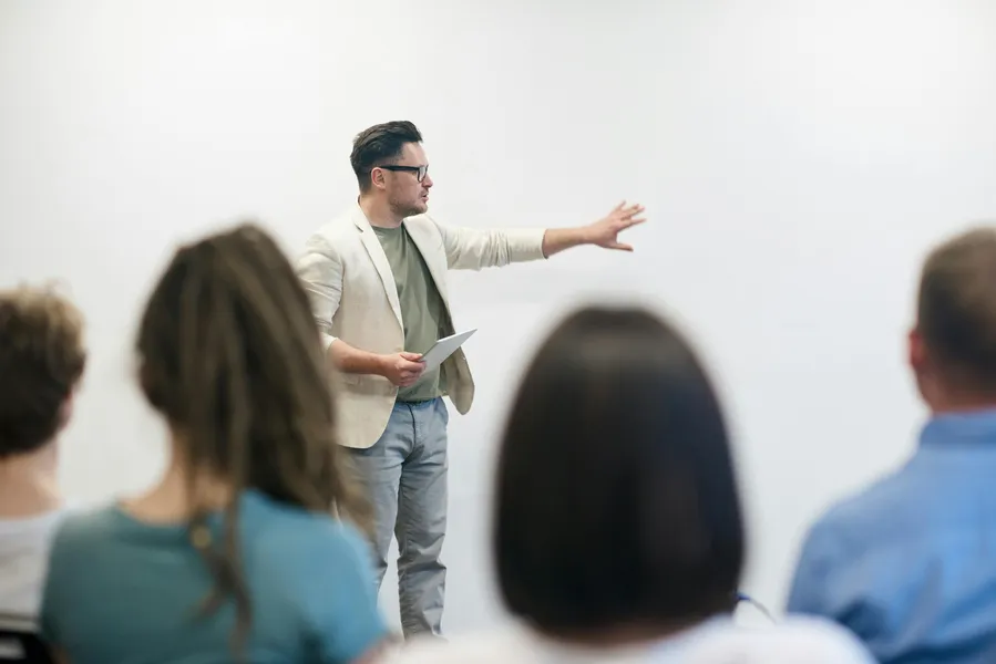 Man standing in front of a class giving a presentation and pointing towards a whiteboard